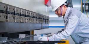 Metal dog-bone specimen loaded into tensile testing machine showing elongation
